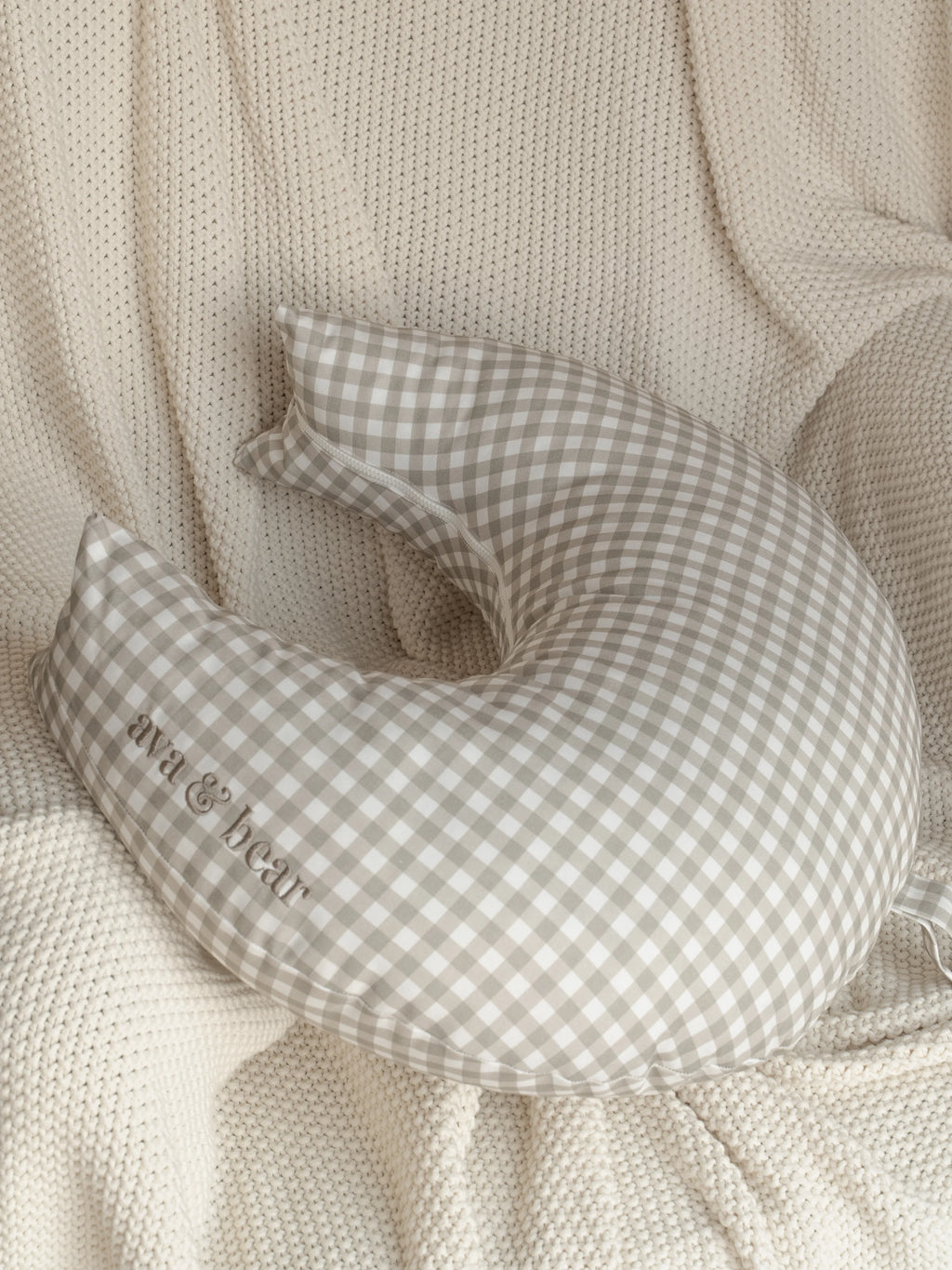 Ava & Bear Ash Brown Gingham Crescent Nursing Cushion elegantly curves around the body, offering optimal support for mother and baby with its 100% cotton twill fabric, eco-friendly design, and convenient loop handle for easy portability.