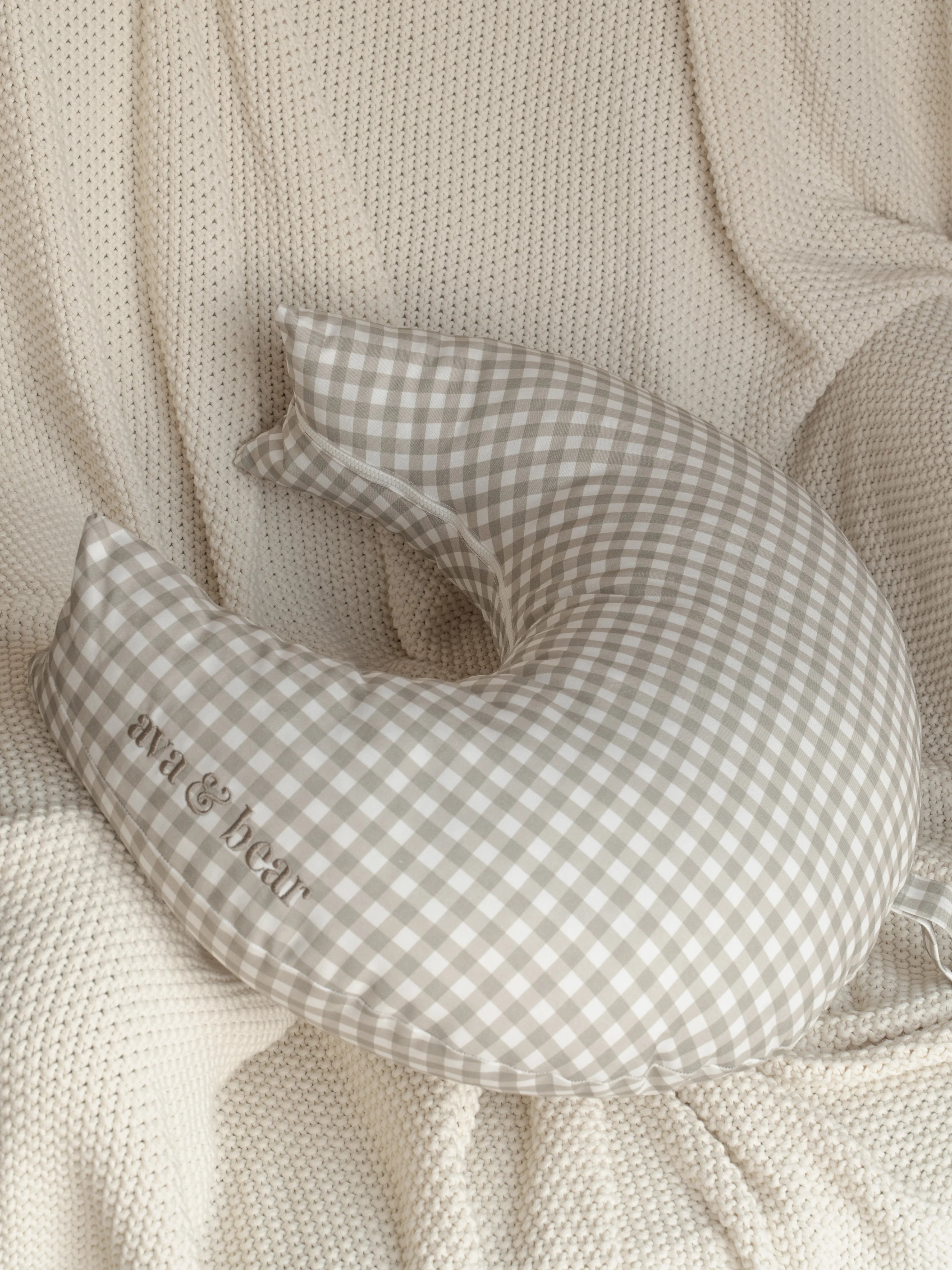 Ava & Bear Ash Brown Gingham Crescent Nursing Cushion elegantly curves around the body, offering optimal support for mother and baby with its 100% cotton twill fabric, eco-friendly design, and convenient loop handle for easy portability.