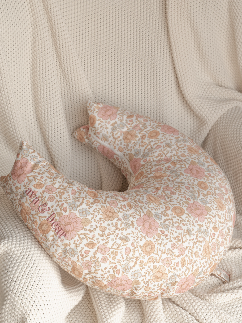 Crescent moon-shaped nursing cushion by Ava & Bear, featuring a dainty floral design, crafted from 100% cotton twill for comfort and durability; ideal for supporting mom and baby during feeding, with a convenient loop handle for easy transport.