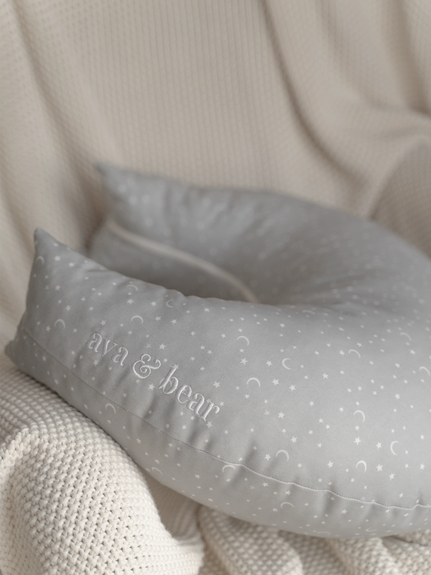 Crescent moon-shaped nursing cushion by Ava & Bear, crafted from 100% cotton twill for durability and comfort, designed to provide optimal support for mom and baby during feeding, with a convenient loop handle for easy portability.