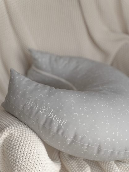 Crescent moon-shaped nursing cushion by Ava & Bear, crafted from 100% cotton twill for durability and comfort, designed to provide optimal support for mom and baby during feeding, with a convenient loop handle for easy portability.
