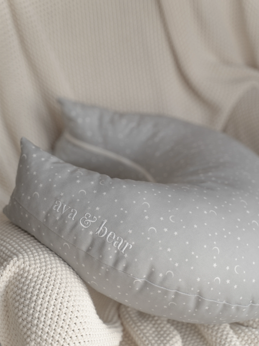 Crescent moon-shaped nursing cushion by Ava & Bear, crafted from 100% cotton twill for durability and comfort, designed to provide optimal support for mom and baby during feeding, with a convenient loop handle for easy portability.